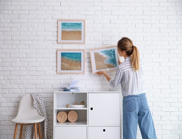 Decorator,Hanging,Picture,On,White,Brick,Wall,In,Room.,Interior